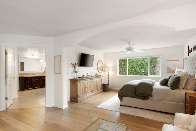 bedroom with connected bathroom, arched walkways, baseboards, and light wood finished floors