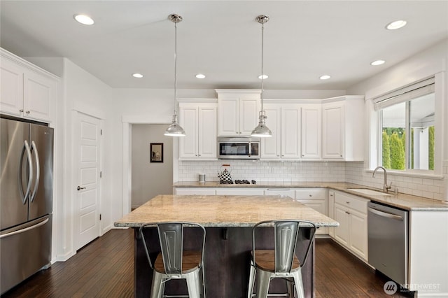 kitchen with dark wood-type flooring, a sink, a kitchen island, white cabinetry, and appliances with stainless steel finishes