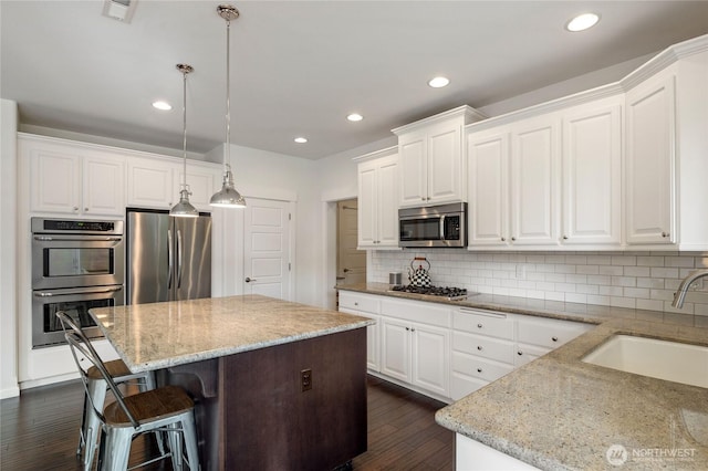 kitchen with light stone counters, dark wood-style floors, a kitchen island, a sink, and stainless steel appliances