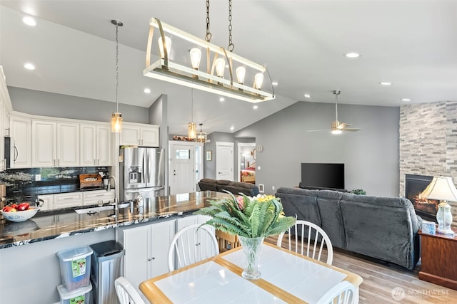 dining space featuring a ceiling fan, light wood-style flooring, vaulted ceiling, a fireplace, and recessed lighting