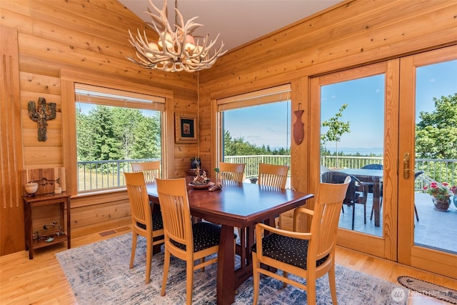 dining area with an inviting chandelier, wooden walls, light wood-style floors, and french doors