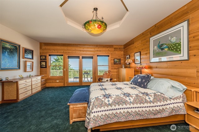 carpeted bedroom with wood walls, access to outside, and a raised ceiling