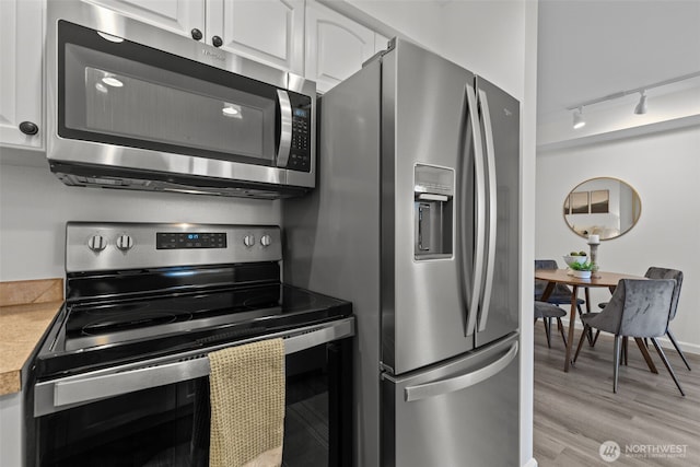 kitchen featuring track lighting, light countertops, light wood-style flooring, appliances with stainless steel finishes, and white cabinetry