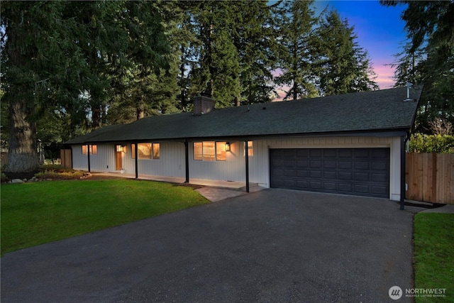 single story home featuring aphalt driveway, a yard, a chimney, fence, and a garage