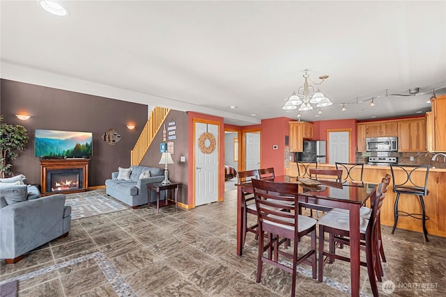 dining area featuring stairway, a notable chandelier, baseboards, and a lit fireplace