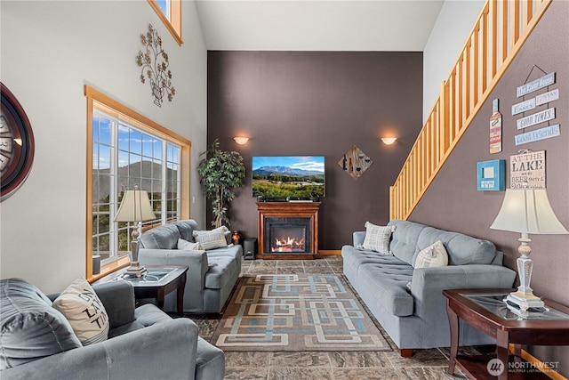 living area with stone finish flooring, a high ceiling, and a glass covered fireplace