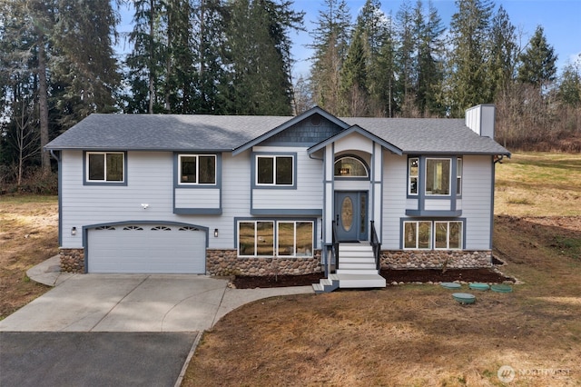 bi-level home with concrete driveway, a garage, stone siding, and a chimney