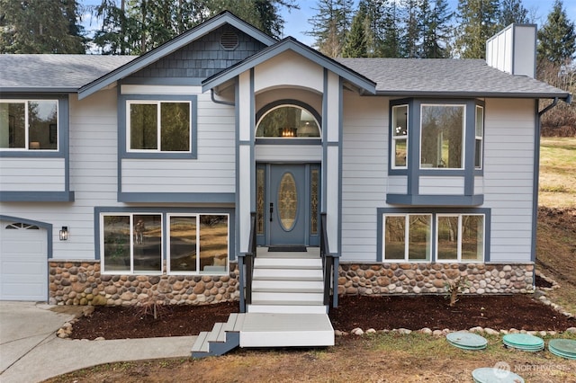 split foyer home featuring stone siding, a chimney, and a shingled roof