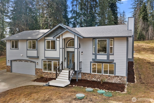 split foyer home featuring stone siding, concrete driveway, a chimney, and an attached garage