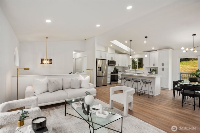 living room featuring an inviting chandelier, recessed lighting, light wood-style floors, and vaulted ceiling