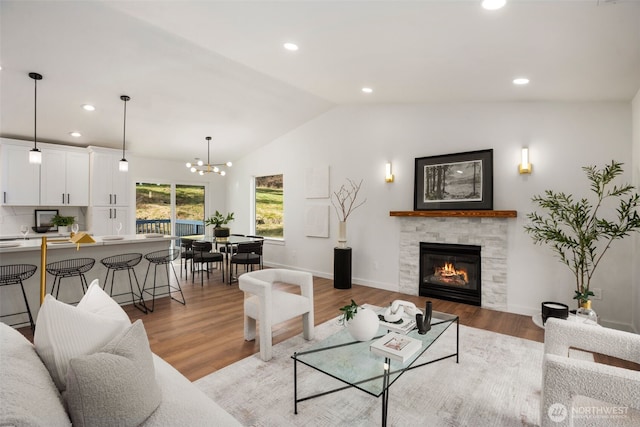 living area featuring a stone fireplace, recessed lighting, light wood-type flooring, and vaulted ceiling