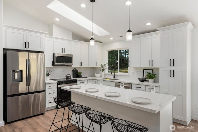 kitchen featuring lofted ceiling with skylight, white cabinetry, stainless steel appliances, and a sink