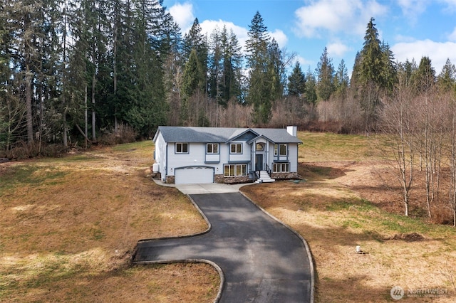 split foyer home featuring aphalt driveway, a garage, a front yard, and a chimney