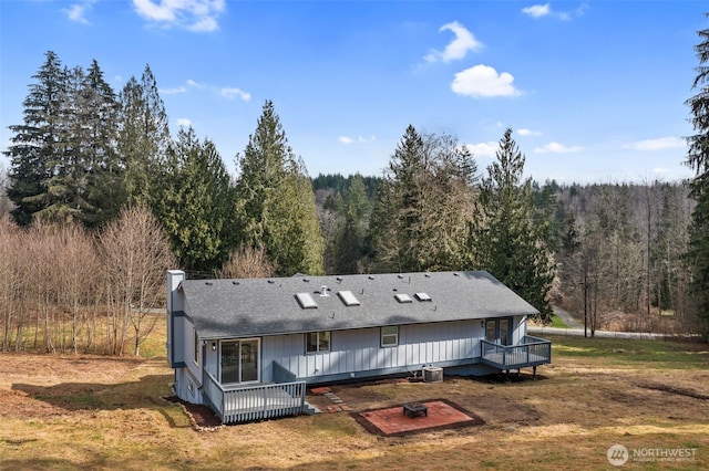 rear view of house with central AC unit, a view of trees, a chimney, and a wooden deck