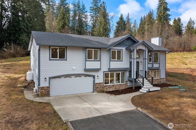 bi-level home featuring concrete driveway, stone siding, and a chimney