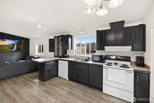 kitchen with white appliances, a peninsula, light countertops, under cabinet range hood, and a sink