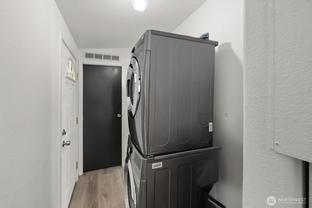 washroom with a textured wall, laundry area, stacked washer / dryer, visible vents, and light wood-style floors