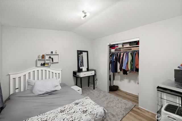 bedroom featuring lofted ceiling, a closet, wood finished floors, and a textured ceiling