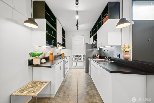 kitchen with dark countertops, tasteful backsplash, appliances with stainless steel finishes, white cabinetry, and a sink