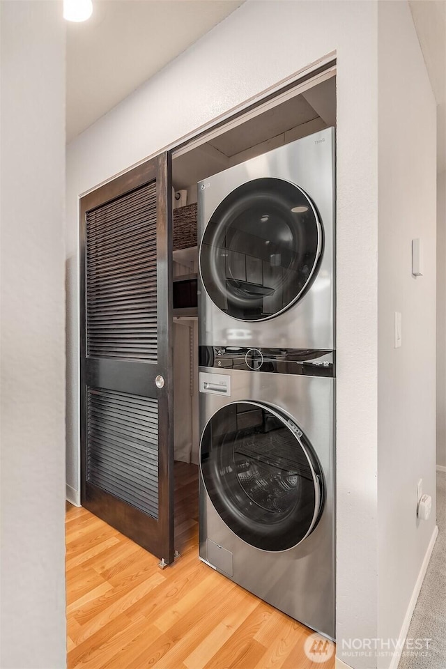 washroom featuring laundry area, stacked washing maching and dryer, wood finished floors, and baseboards