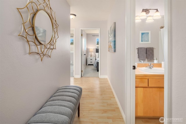 hallway featuring light wood-style floors, a sink, and baseboards