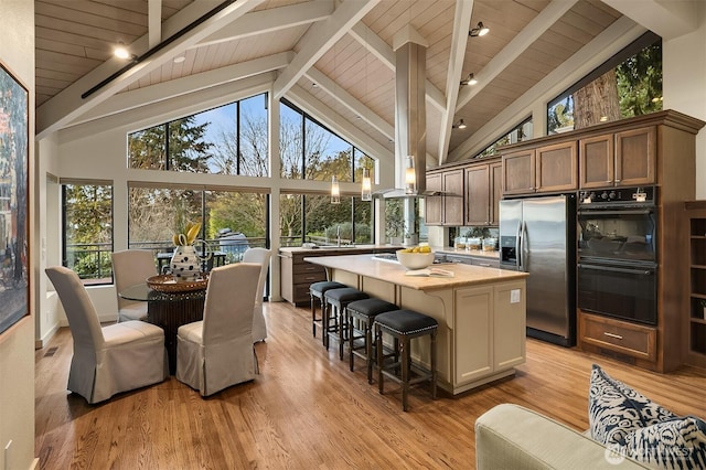 kitchen with a center island, stainless steel fridge with ice dispenser, a breakfast bar area, light wood-type flooring, and dobule oven black