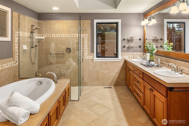 full bath with double vanity, a stall shower, a sink, tile walls, and a bath