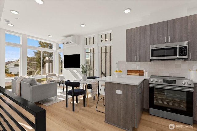 kitchen featuring stainless steel appliances, a peninsula, open floor plan, light countertops, and a wall mounted air conditioner