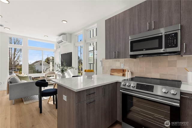 kitchen with stainless steel appliances, tasteful backsplash, an AC wall unit, dark brown cabinets, and a peninsula