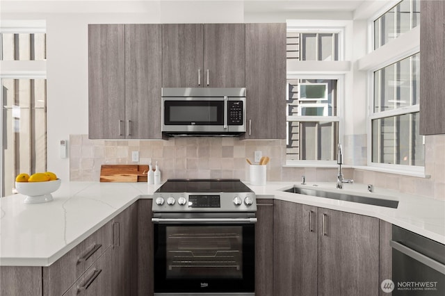 kitchen featuring tasteful backsplash, modern cabinets, appliances with stainless steel finishes, light stone counters, and a sink