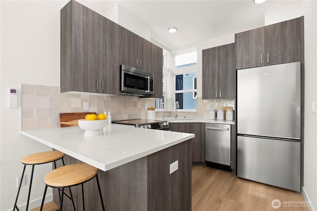 kitchen with appliances with stainless steel finishes, a breakfast bar, dark brown cabinetry, and a peninsula