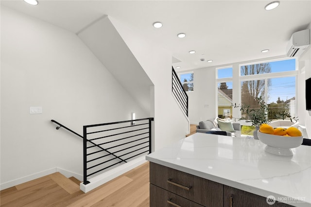 kitchen with a wall unit AC, recessed lighting, baseboards, light wood-type flooring, and light stone countertops