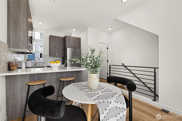 kitchen with a breakfast bar area, tasteful backsplash, light countertops, dark brown cabinets, and a peninsula