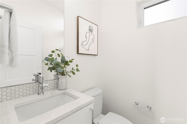 half bath with backsplash, vanity, and toilet