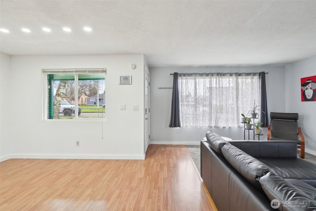 living area featuring light wood-style floors, baseboards, a wealth of natural light, and a textured ceiling