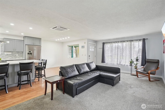 living room with a textured ceiling, a healthy amount of sunlight, visible vents, and baseboards