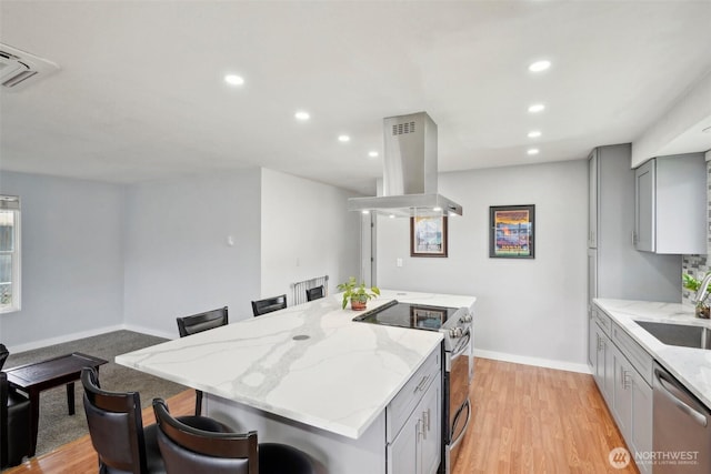 kitchen featuring a breakfast bar area, a sink, gray cabinetry, appliances with stainless steel finishes, and island range hood