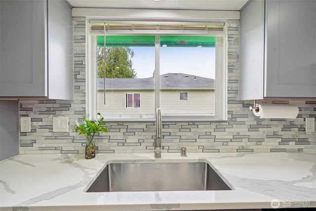 kitchen featuring tasteful backsplash, gray cabinets, light stone counters, and a sink