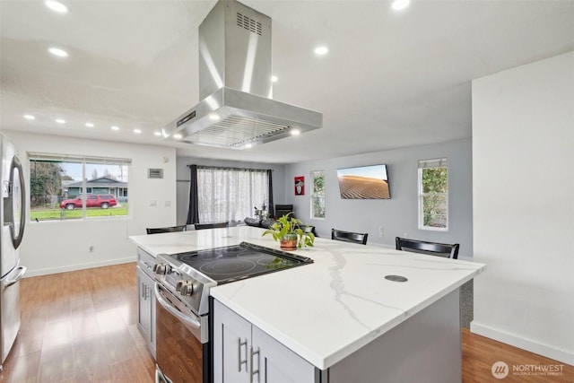 kitchen with a center island, light stone counters, light wood-style flooring, island range hood, and stainless steel appliances