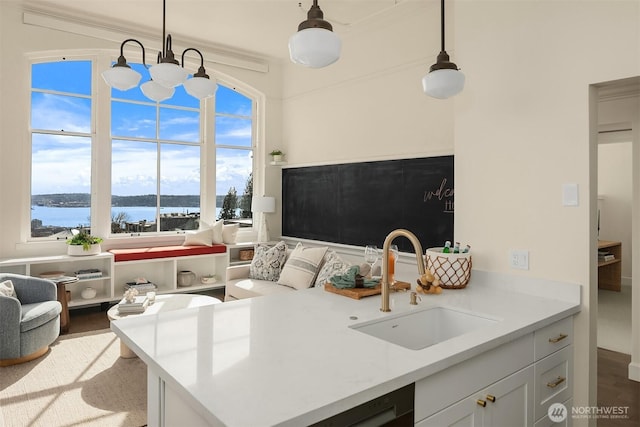 kitchen with a sink, light countertops, white cabinets, a water view, and decorative light fixtures