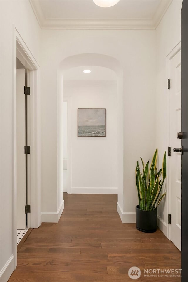 corridor featuring arched walkways, crown molding, baseboards, and wood finished floors