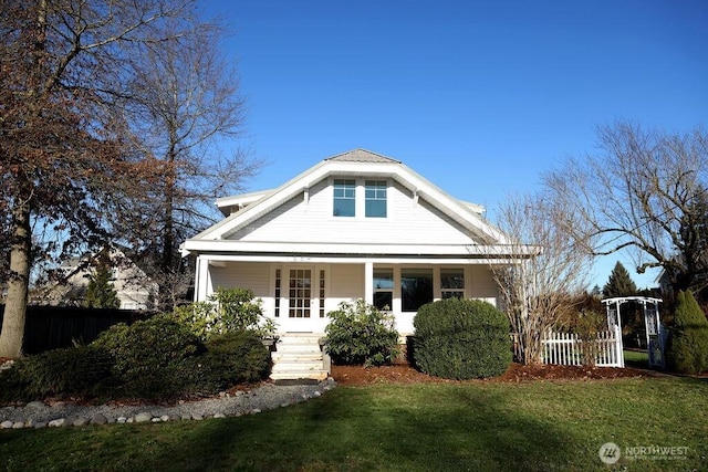 view of front of property featuring covered porch, fence, and a front lawn