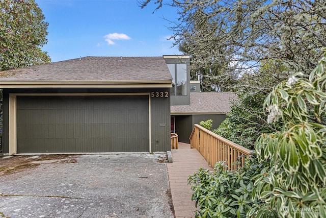 view of front of home featuring driveway, an attached garage, and roof with shingles