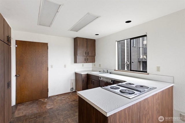 kitchen featuring dishwasher, a peninsula, light countertops, stainless steel electric stovetop, and a sink