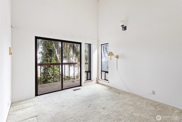 empty room with carpet floors, visible vents, and a high ceiling