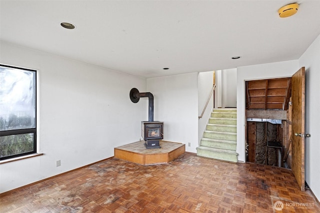 unfurnished living room with stairs, a wood stove, and baseboards