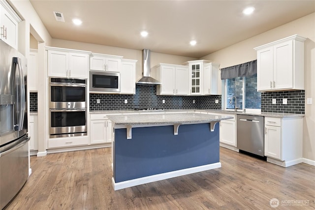 kitchen with appliances with stainless steel finishes, a breakfast bar, white cabinets, and wall chimney range hood