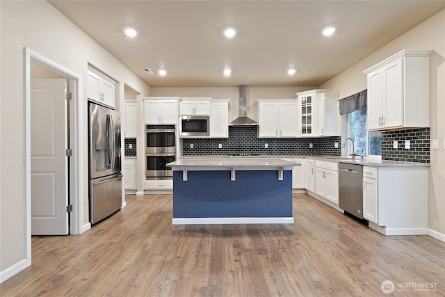 kitchen featuring a kitchen island, wall chimney range hood, a kitchen breakfast bar, appliances with stainless steel finishes, and white cabinetry