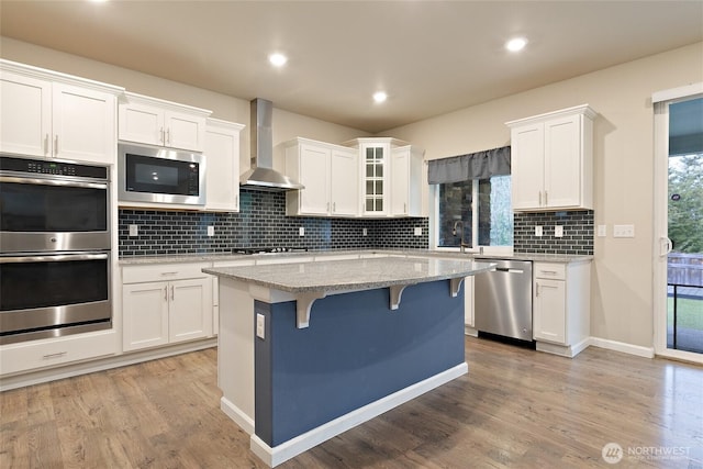 kitchen featuring a breakfast bar area, stainless steel appliances, white cabinetry, wall chimney exhaust hood, and light wood-type flooring