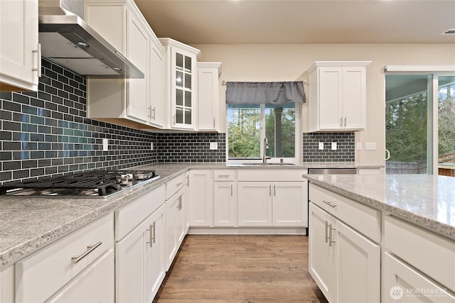 kitchen with stainless steel gas stovetop, white cabinetry, wall chimney exhaust hood, and a sink